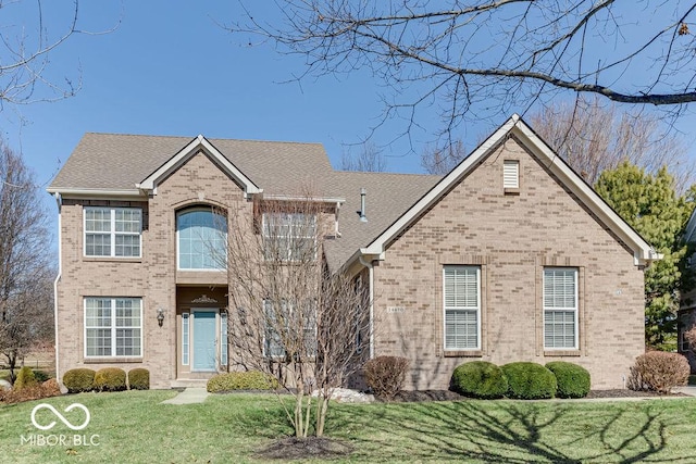 view of front of property featuring a front lawn, brick siding, and roof with shingles