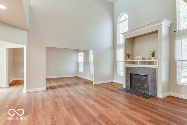 unfurnished living room with a fireplace, baseboards, a towering ceiling, and wood finished floors