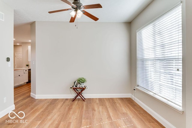 spare room with baseboards, light wood-style floors, and a ceiling fan