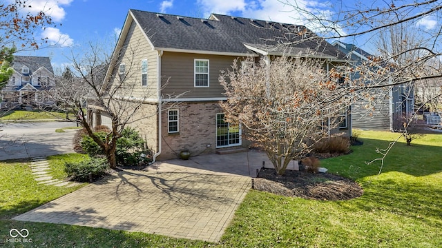 back of house with a patio, roof with shingles, a yard, decorative driveway, and brick siding