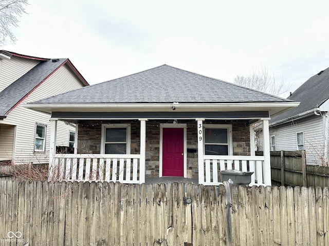 bungalow-style house featuring stone siding, roof with shingles, covered porch, and fence