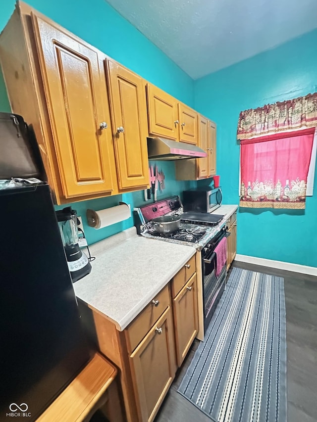 kitchen with black appliances, under cabinet range hood, light countertops, baseboards, and dark wood-style flooring