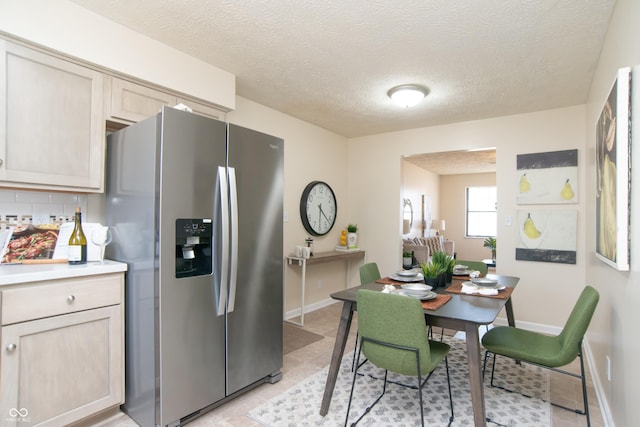 kitchen with decorative backsplash, light countertops, baseboards, and stainless steel refrigerator with ice dispenser