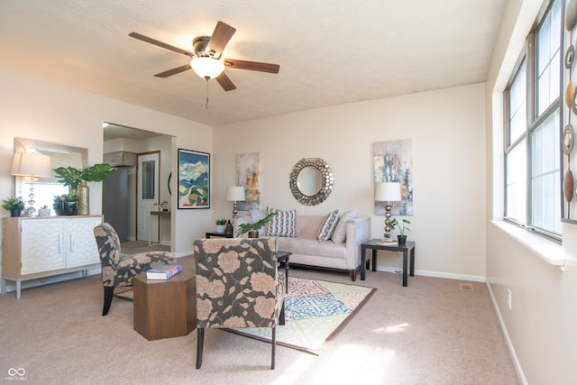 living area featuring visible vents, baseboards, light colored carpet, a textured ceiling, and a ceiling fan