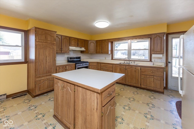 kitchen with light floors, stainless steel gas range, a kitchen island, a sink, and under cabinet range hood