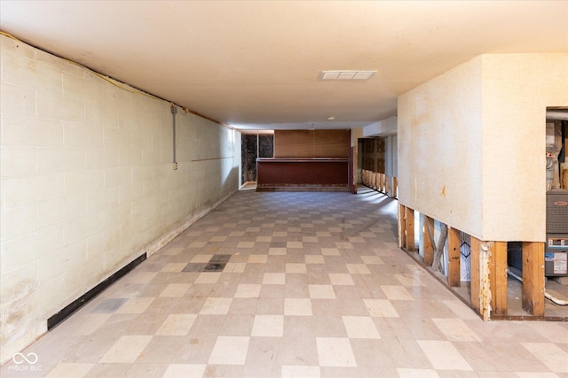 hallway with concrete block wall, light floors, and visible vents