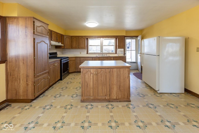 kitchen featuring freestanding refrigerator, a sink, under cabinet range hood, stainless steel gas range oven, and a center island