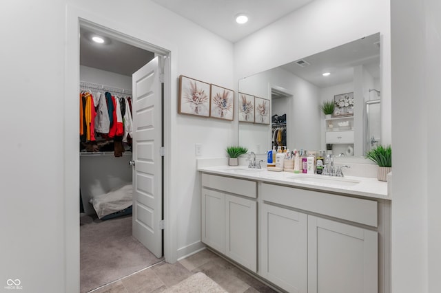 bathroom with a walk in closet, double vanity, recessed lighting, and a sink