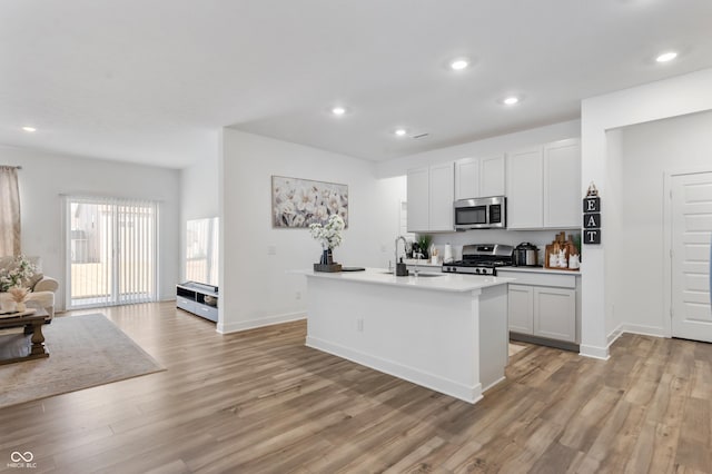 kitchen with recessed lighting, a center island with sink, light wood finished floors, and stainless steel appliances