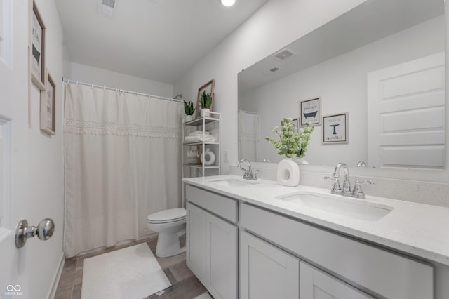 bathroom featuring double vanity, visible vents, toilet, and a sink