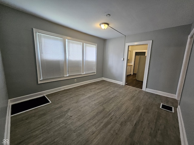 unfurnished bedroom with dark wood-style floors, visible vents, and baseboards