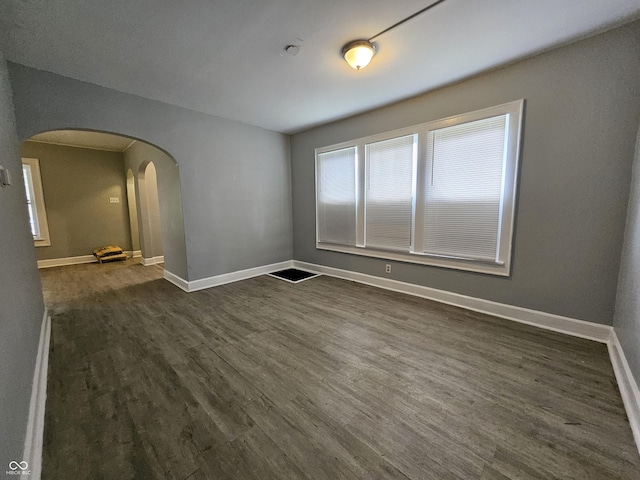 empty room featuring baseboards, arched walkways, and dark wood-style flooring