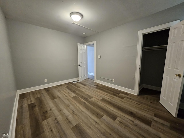 unfurnished bedroom featuring dark wood finished floors, visible vents, a closet, and baseboards