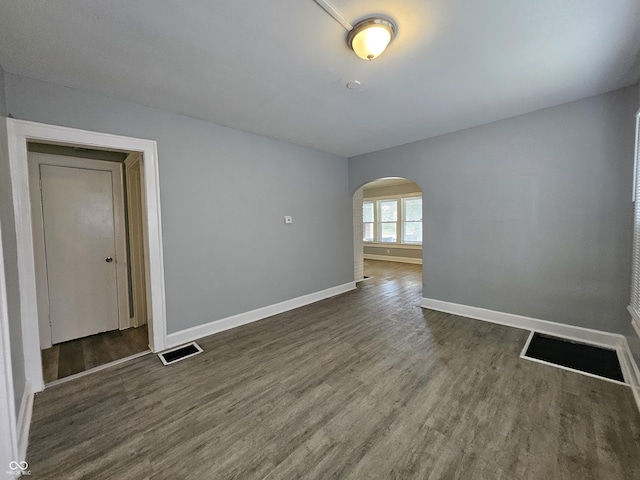 spare room with arched walkways, visible vents, dark wood finished floors, and baseboards