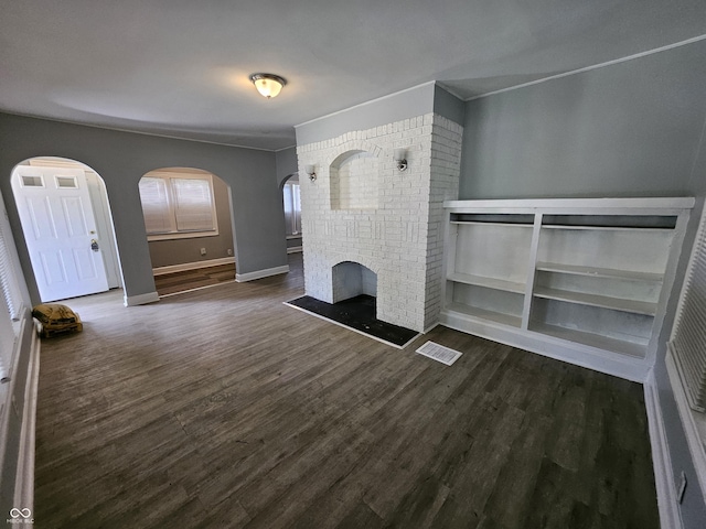 unfurnished living room featuring visible vents, arched walkways, a brick fireplace, and wood finished floors