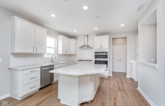 kitchen with visible vents, white cabinets, stainless steel appliances, wall chimney exhaust hood, and a sink