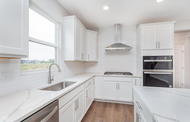 kitchen featuring white cabinets, wall chimney exhaust hood, stainless steel appliances, and a sink