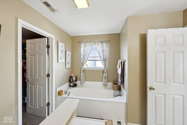 bathroom with a garden tub, visible vents, and a textured ceiling