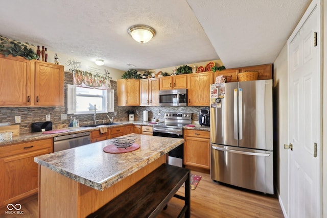 kitchen with light wood-style flooring, a sink, appliances with stainless steel finishes, a kitchen bar, and tasteful backsplash