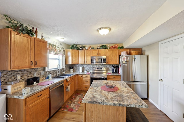 kitchen featuring tasteful backsplash, a kitchen island, appliances with stainless steel finishes, light wood-style floors, and a sink