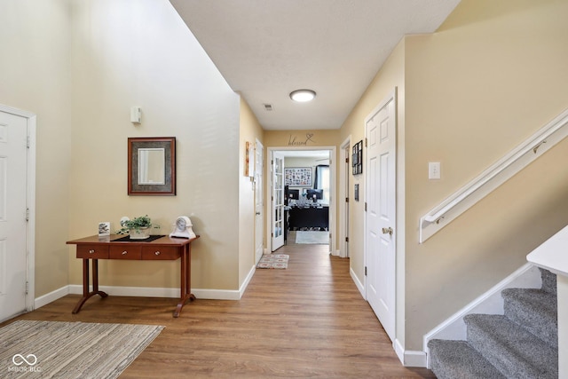 corridor featuring light wood-type flooring, baseboards, and stairs