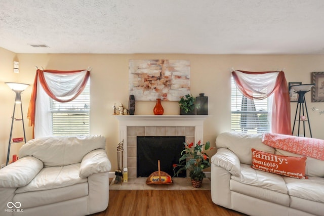 living area featuring visible vents, a textured ceiling, wood finished floors, and a tiled fireplace