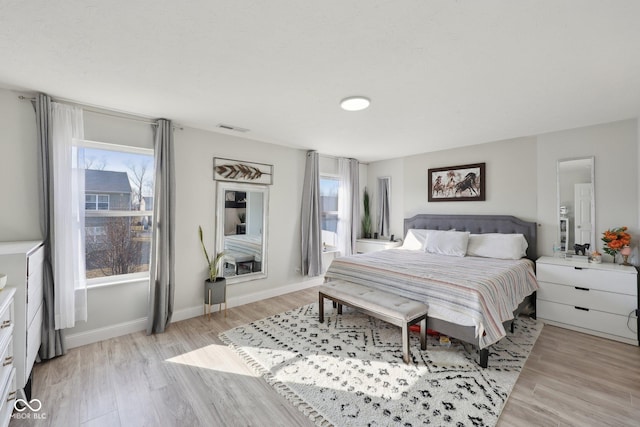 bedroom with visible vents, multiple windows, light wood-type flooring, and baseboards