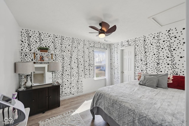 bedroom featuring a ceiling fan, attic access, wood finished floors, and baseboards