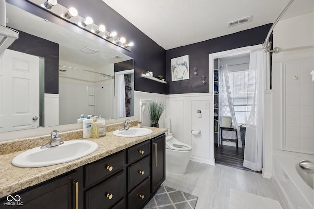 full bathroom with a sink, toilet, double vanity, and wainscoting