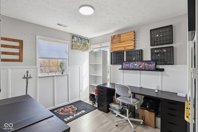 office with a textured ceiling, wood finished floors, visible vents, and wainscoting