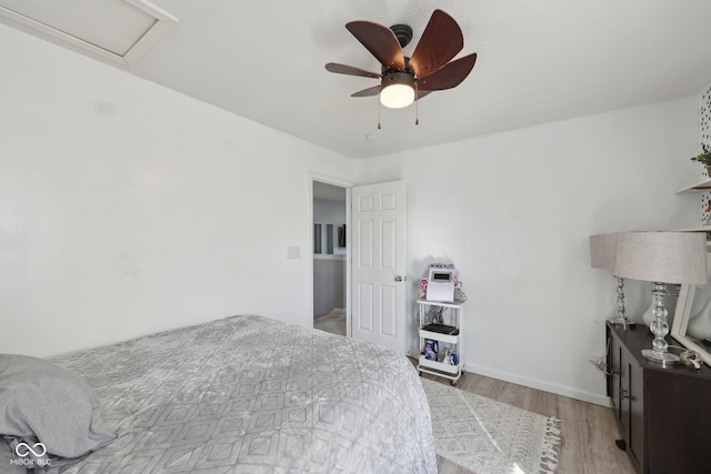 bedroom with attic access, a ceiling fan, baseboards, and light wood finished floors