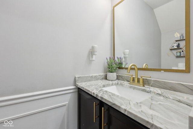 bathroom with a wainscoted wall, vanity, and vaulted ceiling