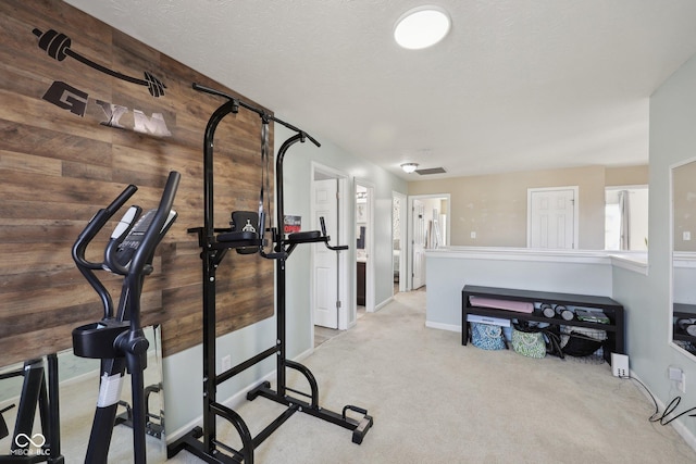 exercise room featuring carpet flooring, wood walls, and a textured ceiling