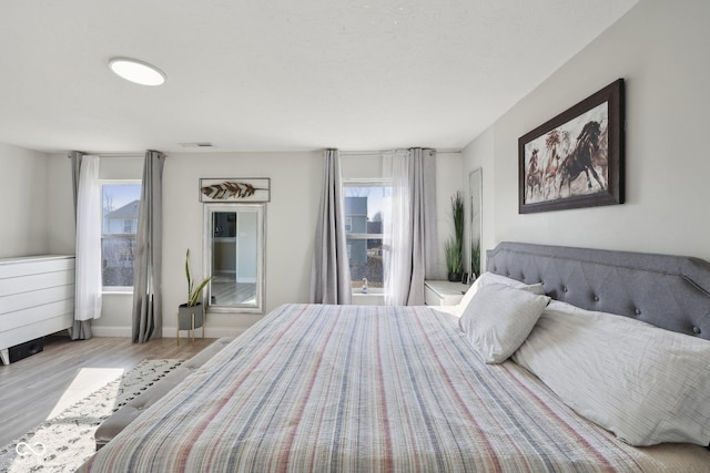 bedroom featuring visible vents, multiple windows, baseboards, and wood finished floors