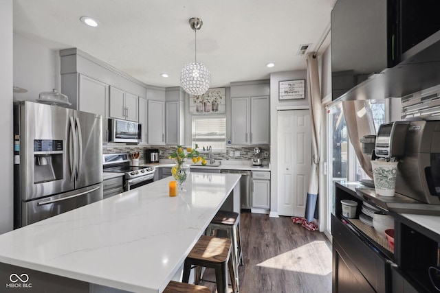 kitchen featuring visible vents, tasteful backsplash, dark wood-style floors, appliances with stainless steel finishes, and a breakfast bar area