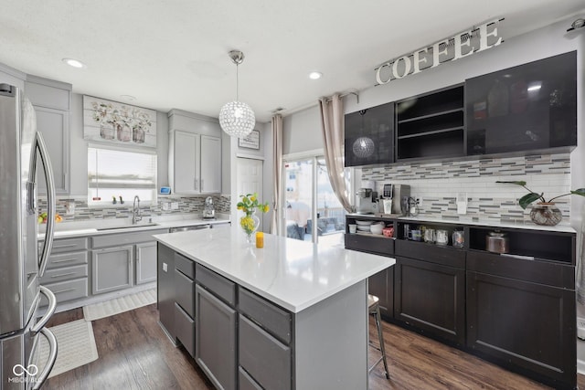 kitchen featuring dark wood-type flooring, gray cabinets, a sink, a kitchen island, and stainless steel fridge