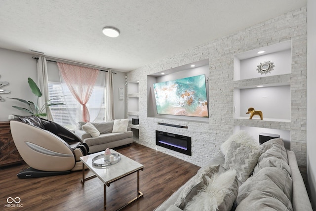 living room with visible vents, built in shelves, a textured ceiling, wood finished floors, and a glass covered fireplace