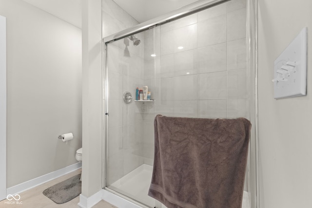 bathroom featuring toilet, baseboards, and a stall shower