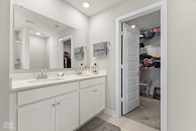 bathroom featuring double vanity, visible vents, a walk in closet, and a sink