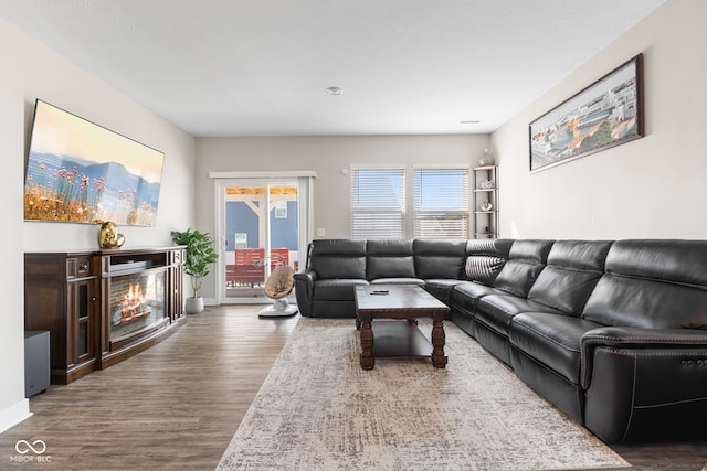 living room featuring a glass covered fireplace, baseboards, and wood finished floors