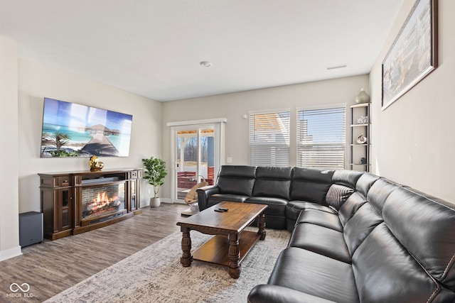 living room featuring a glass covered fireplace, wood finished floors, visible vents, and baseboards