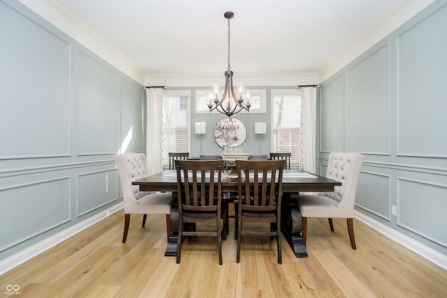 dining room with light wood-type flooring, an inviting chandelier, crown molding, and a decorative wall