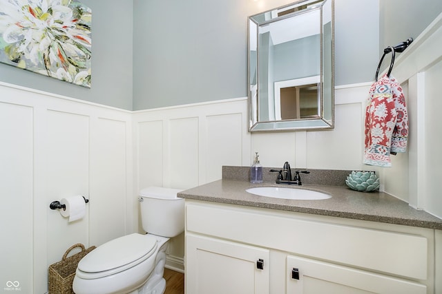 bathroom with a decorative wall, wainscoting, toilet, and vanity