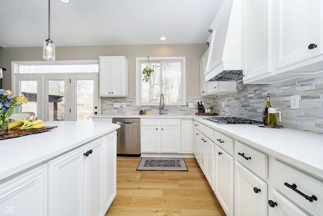 kitchen featuring light wood finished floors, custom exhaust hood, a sink, stainless steel appliances, and white cabinetry