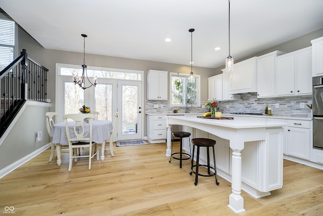 kitchen with a kitchen island, light wood-style flooring, a sink, light countertops, and custom range hood