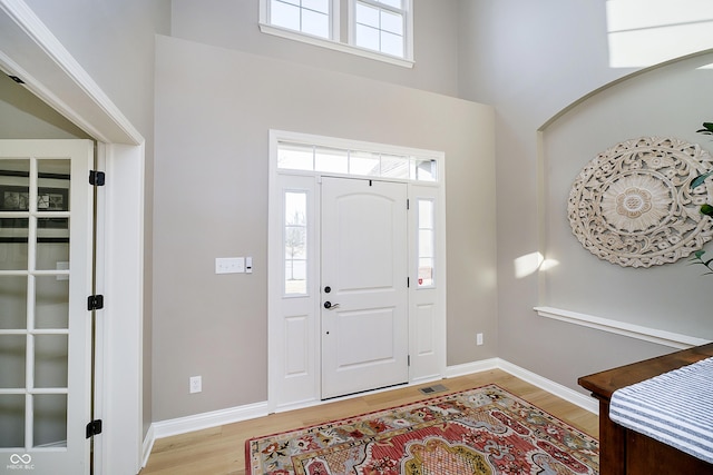 foyer entrance with a wealth of natural light, baseboards, a towering ceiling, and light wood finished floors