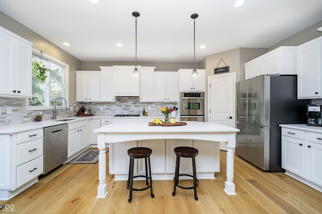 kitchen with a sink, a center island, light wood-style floors, appliances with stainless steel finishes, and a breakfast bar area