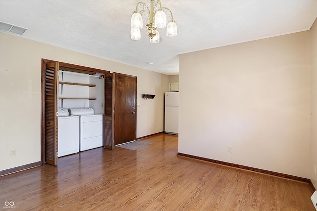 empty room featuring wood finished floors, baseboards, a textured ceiling, washer and dryer, and a chandelier