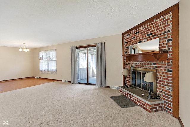 carpeted living room featuring baseboards, visible vents, a textured ceiling, a brick fireplace, and a chandelier