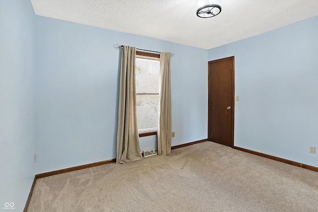 spare room featuring a textured ceiling, light colored carpet, visible vents, and baseboards